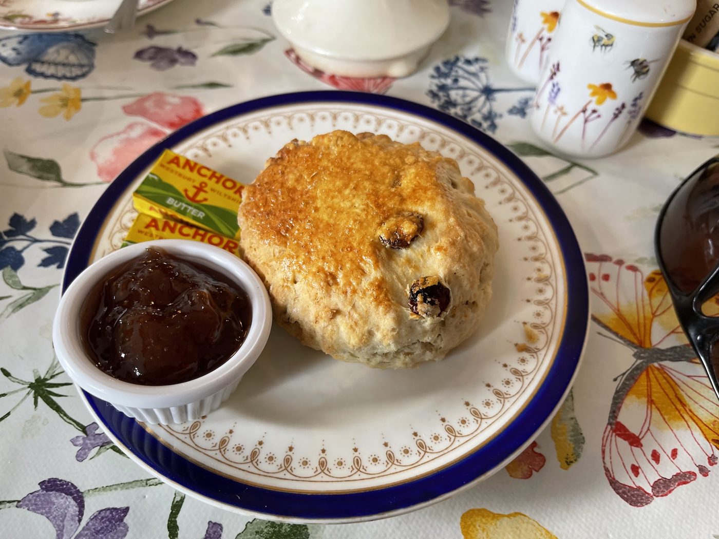 A fruit scone with a pot of jam on a blue-rimmed plate