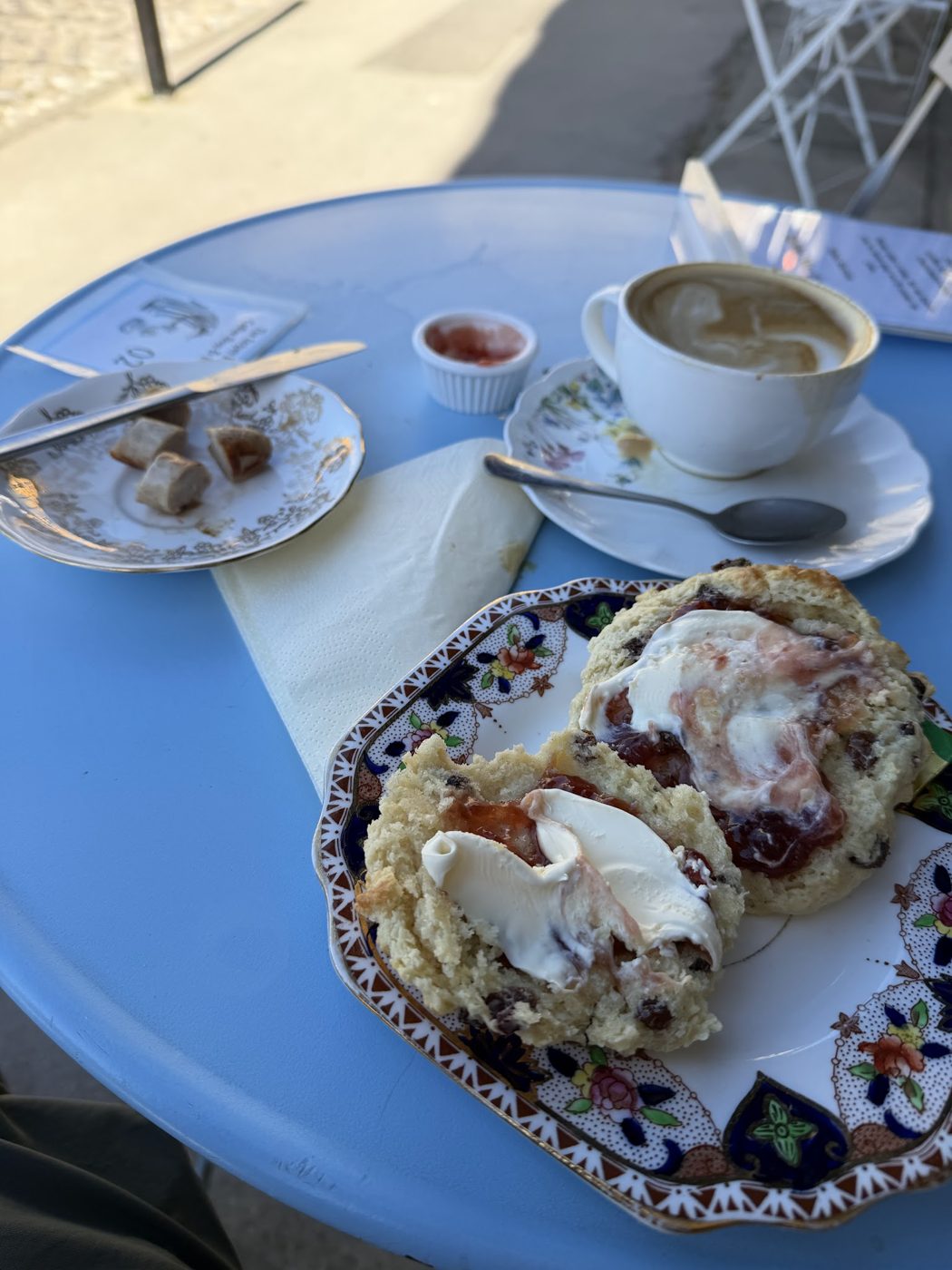 Scones with cream and jam beside a cup on a blue table
